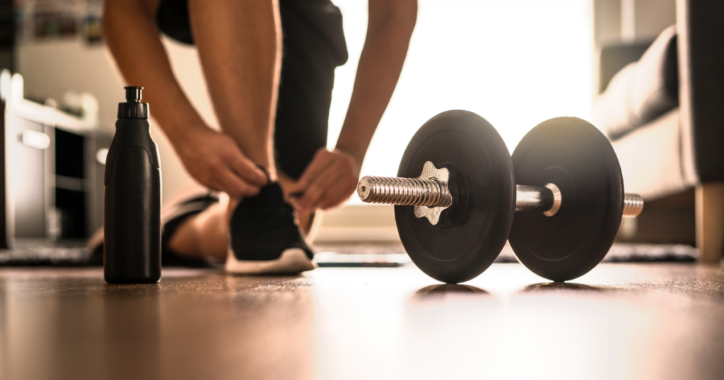 person tying shoe in front of dumbbell